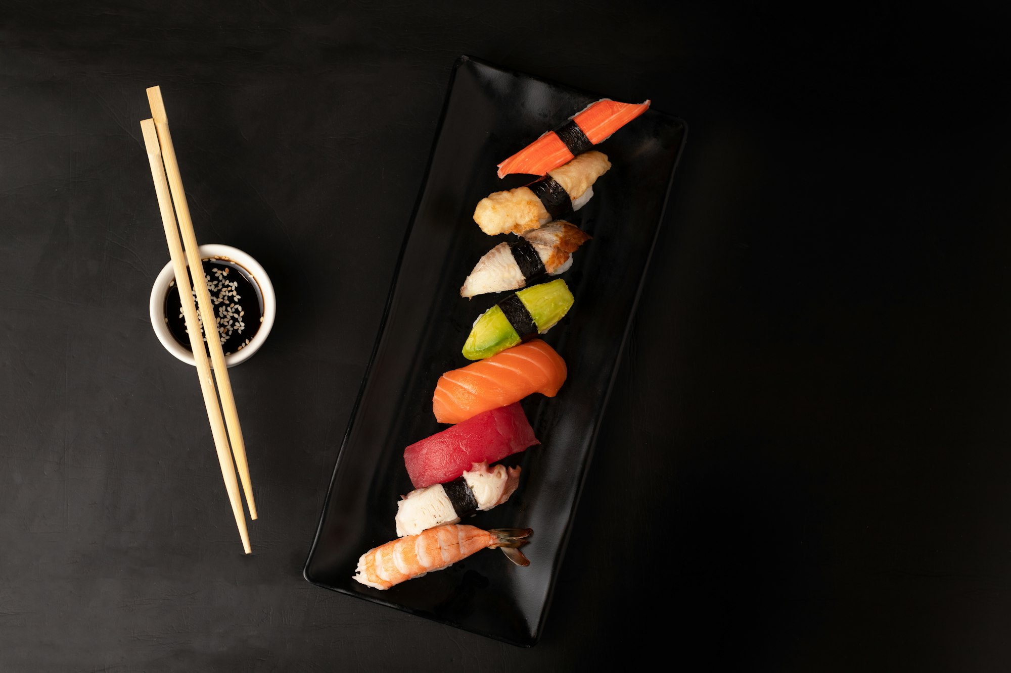 An arrangement of nigiri sushi plated on matte black slate